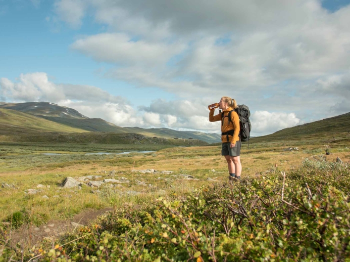 Kvinna med ryggsäck står i fjällen och dricker ur vattenflaska.