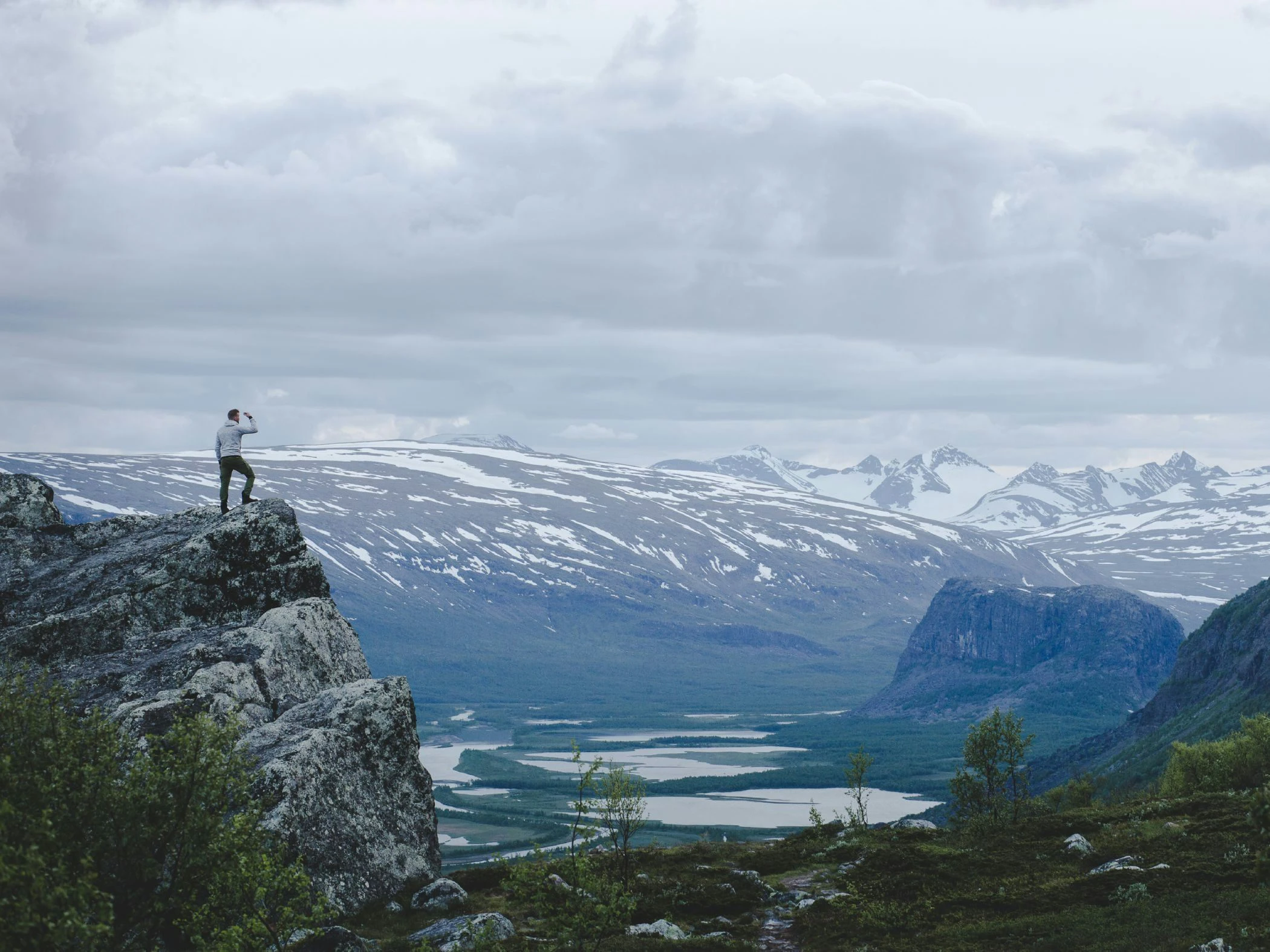 En ensam vandrare som spanar ut över fjällandskap och sjöar från en brant klippa.