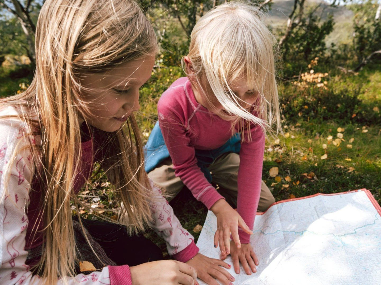 Två barn sitter utomhus i naturen och tittar på en karta tillsammans.
