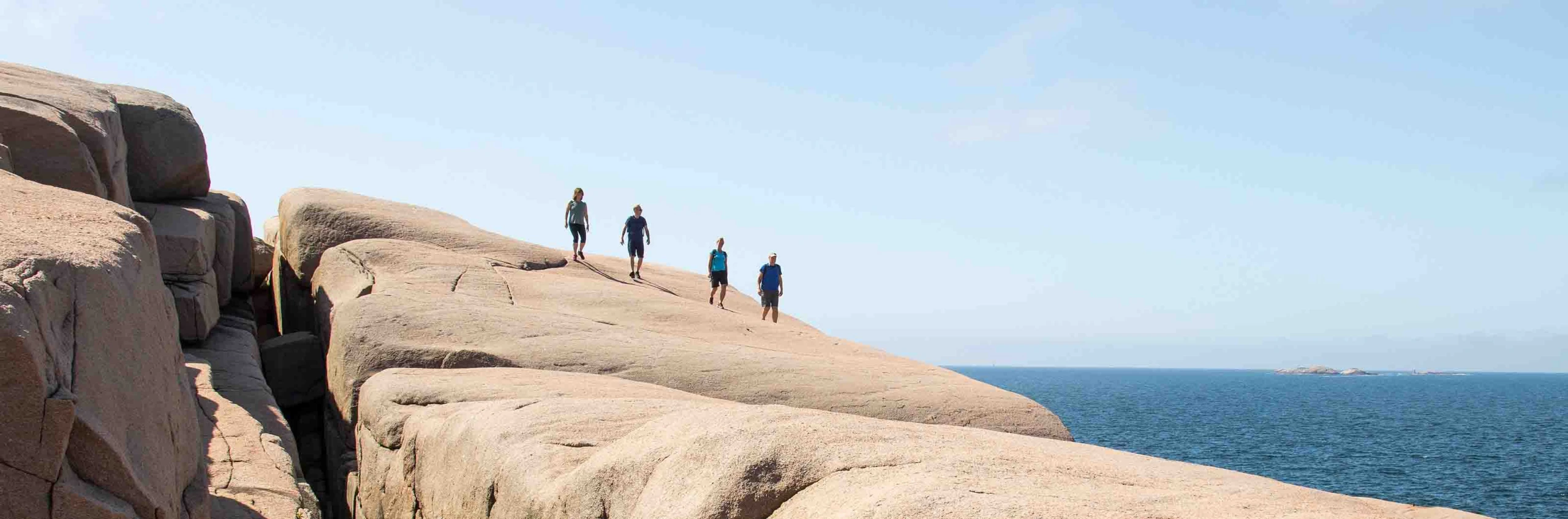Fyra vandrare på släta klippor vid havet under klar himmel.