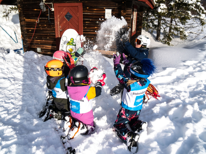Barn leker i snön utanför en stuga på vintern.