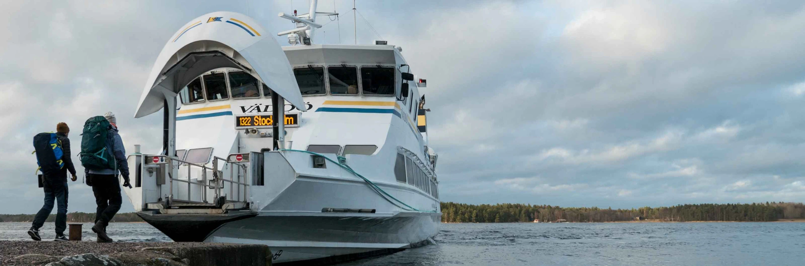 Två vandrare går ombord på en skärgårdsfärja vid kajen.