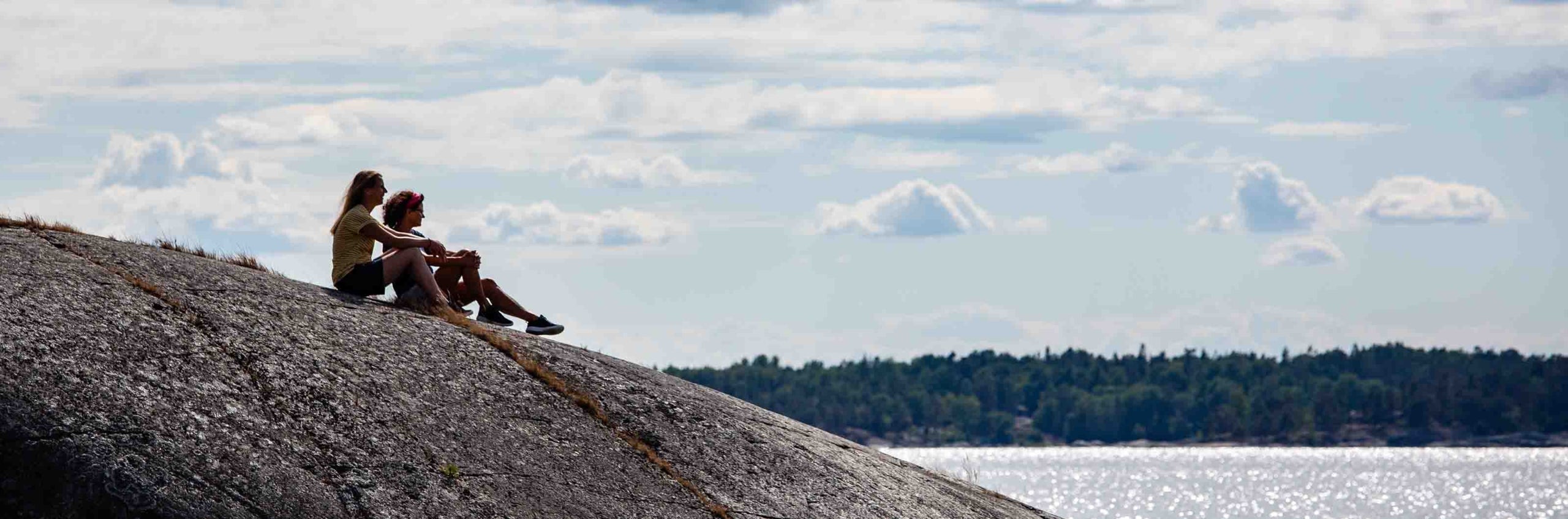 Två personer sitter på en klippa med utsikt över havet.