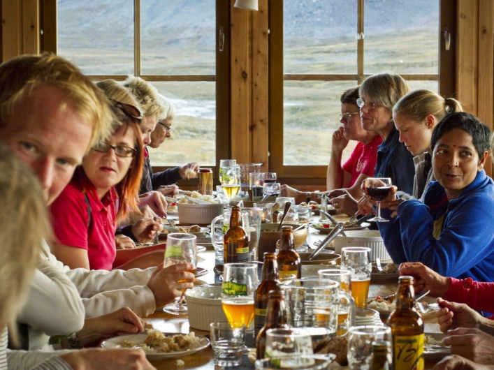 En grupp människor som sitter runt ett bord och äter mat på Sylarnas Fjällstation.