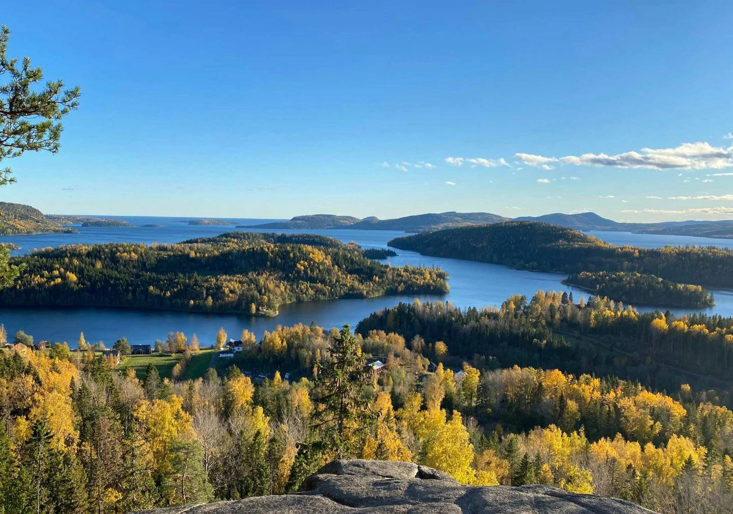 Utsikt över skärgårdsliknande sjölandskap med öar, skog i höstfärger och klart blå himmel.