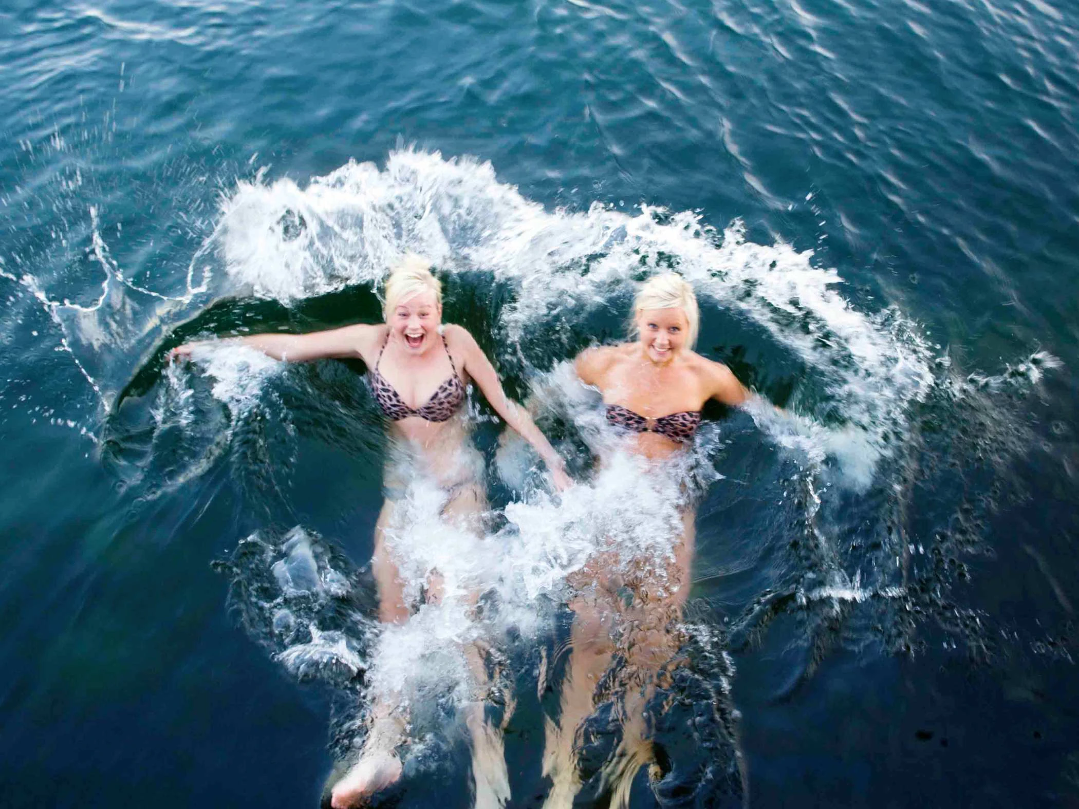Två tjejer som slänger sig bakåt ner i havet och ser glada ut över ett kallbad.