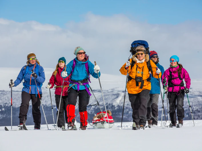 En grupp åker turskidor med fjällpulka i snötäckt landskap.