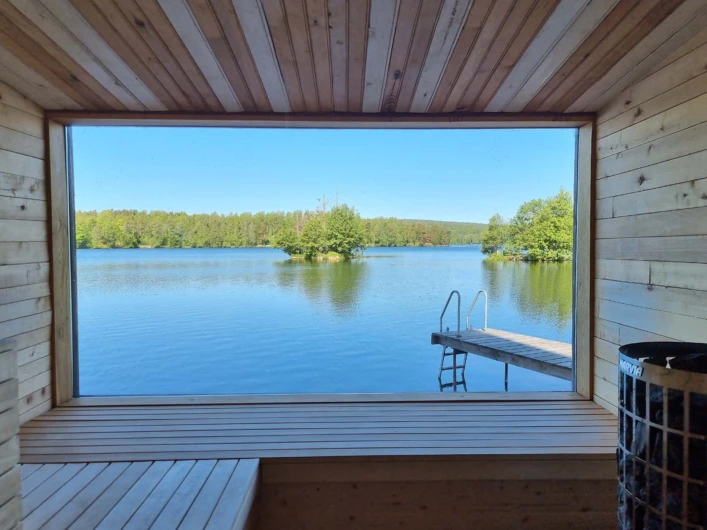 Utsikt från en bastu över en lugn sjö med brygga och små gröna öar.