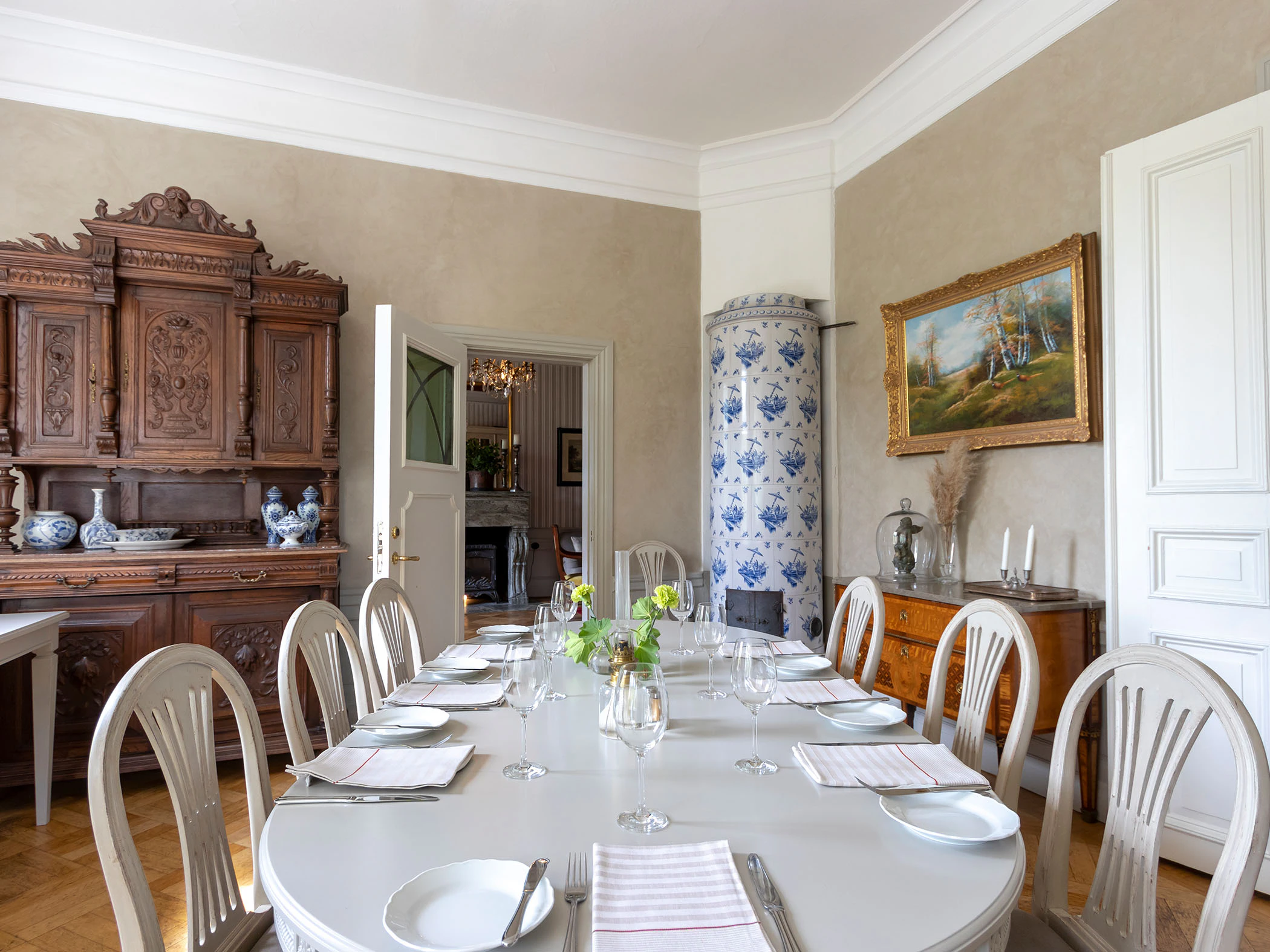 Matsal med dukat bord, kakelugn och klassiska trämöbler.