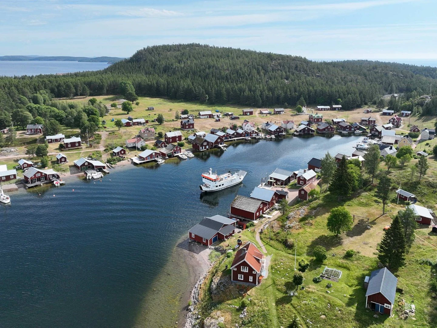 Flygvy över kustby med röda hus, bryggor och båt i en skyddad vik.