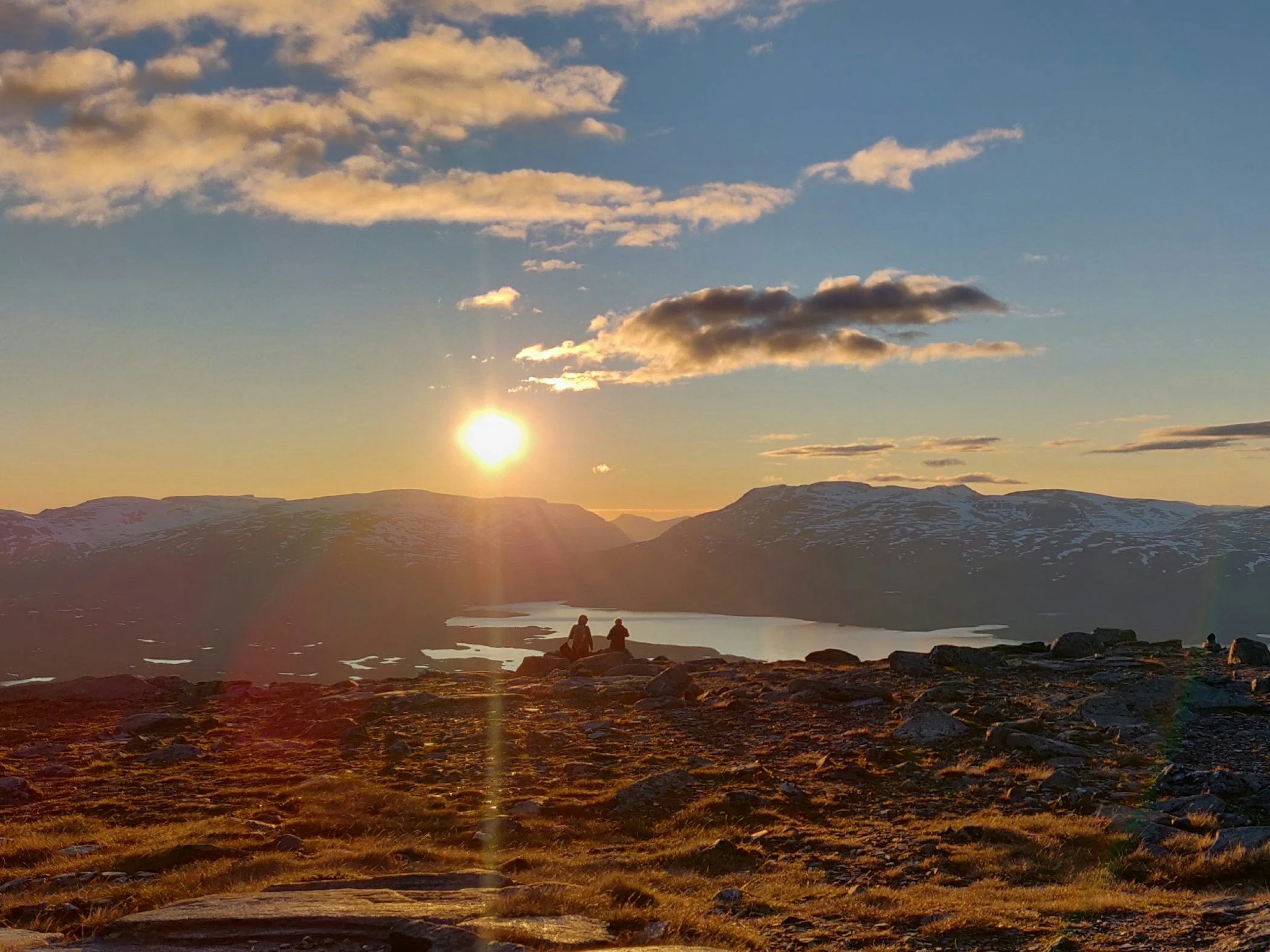 Två personer tittar på solnedgången på ett berg i vacker fjällmiljö.