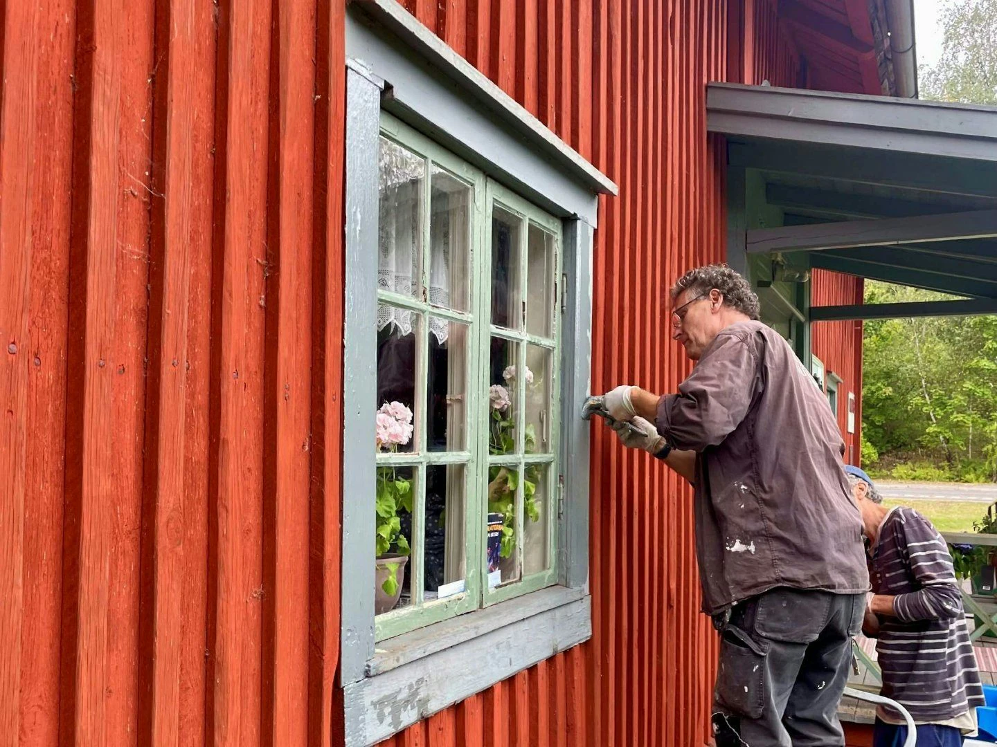 En man skrapar färg på ett fönster på ett gammalt hus.