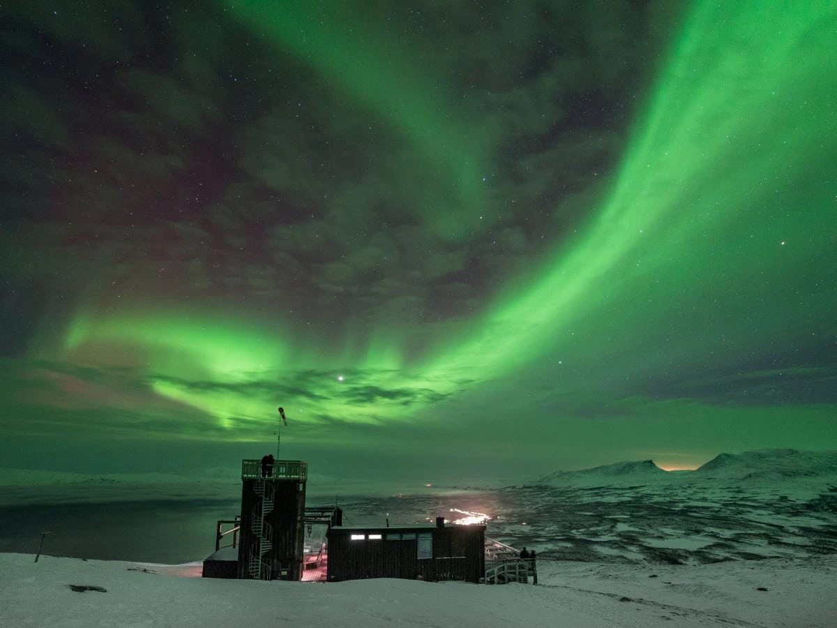 Aurora Sky Station i Abisko under ett starkt norrsken över det snötäckta fjällandskapet.