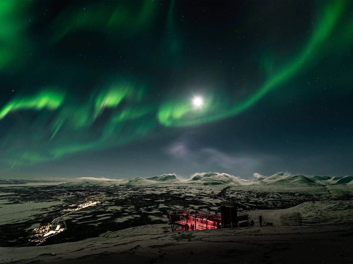 Norrsken och månsken över det snötäckta fjällandskapet vid Aurora Sky Station i Abisko.