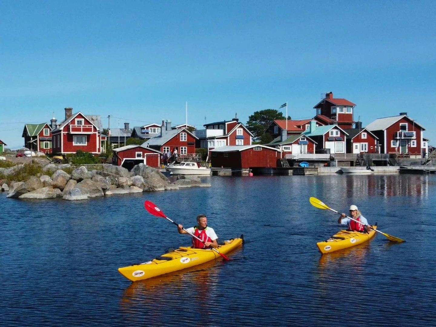 Två personer som paddlar i gula kajaker i skärgården.