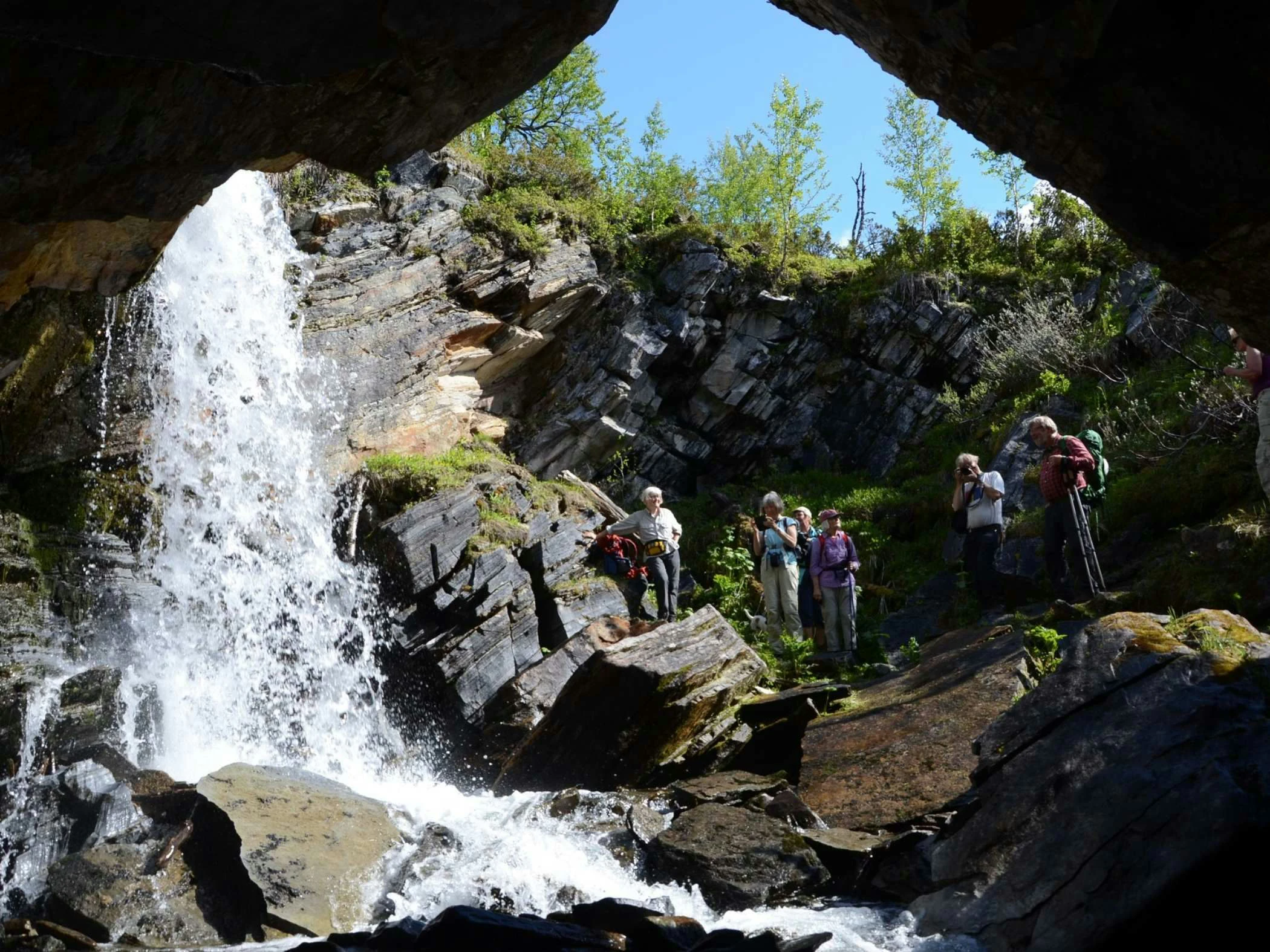 Vandrare står vid ett vattenfall i en klippig ravin och betraktar naturen.
