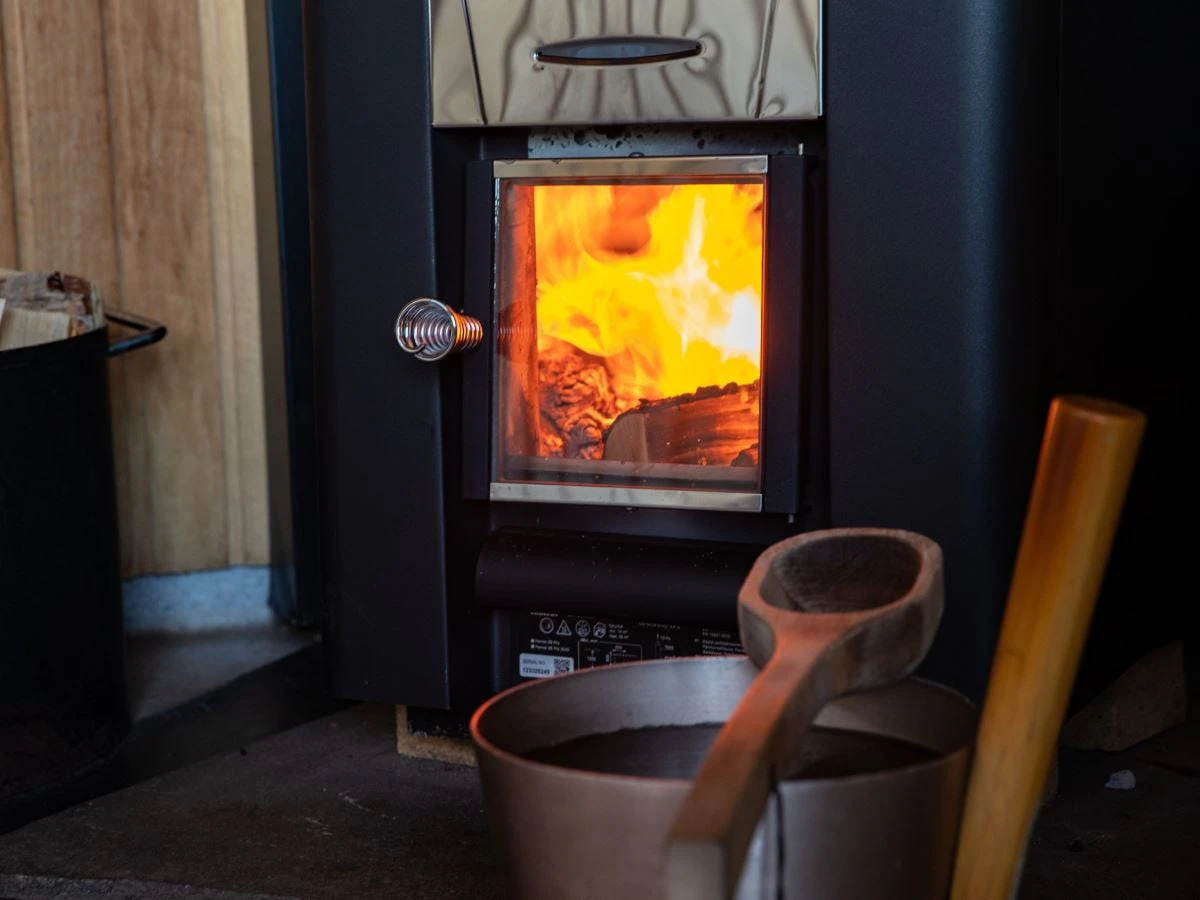 Vedeldad kamin med brinnande eld och bastuhink i förgrunden.