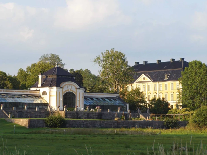 Orangeriet och Nynäs slott omgivna av grönska i kvällssol.